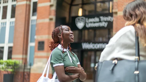 Two students talking and laughing outside the Leeds City Campus entrance.
